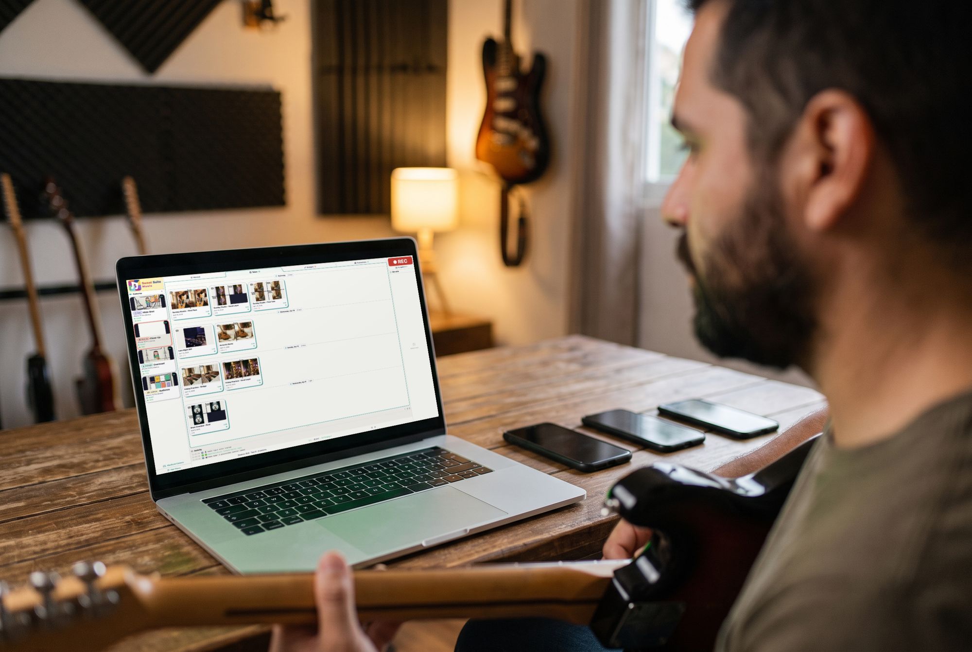 A guitarist at his desk looks over his takes on his Mac, his phones laid out beside it